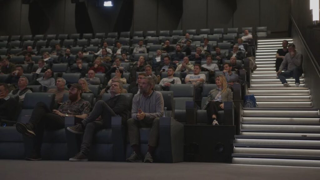 Personer i samtale under netværksarrangement i Lyngby med kameraudstyr og lysopsætning i baggrunden – fokus på videoproduktion og samarbejde
